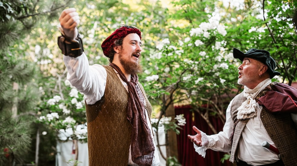 Two actors wearing period dress, performing in an outdoor theatre
